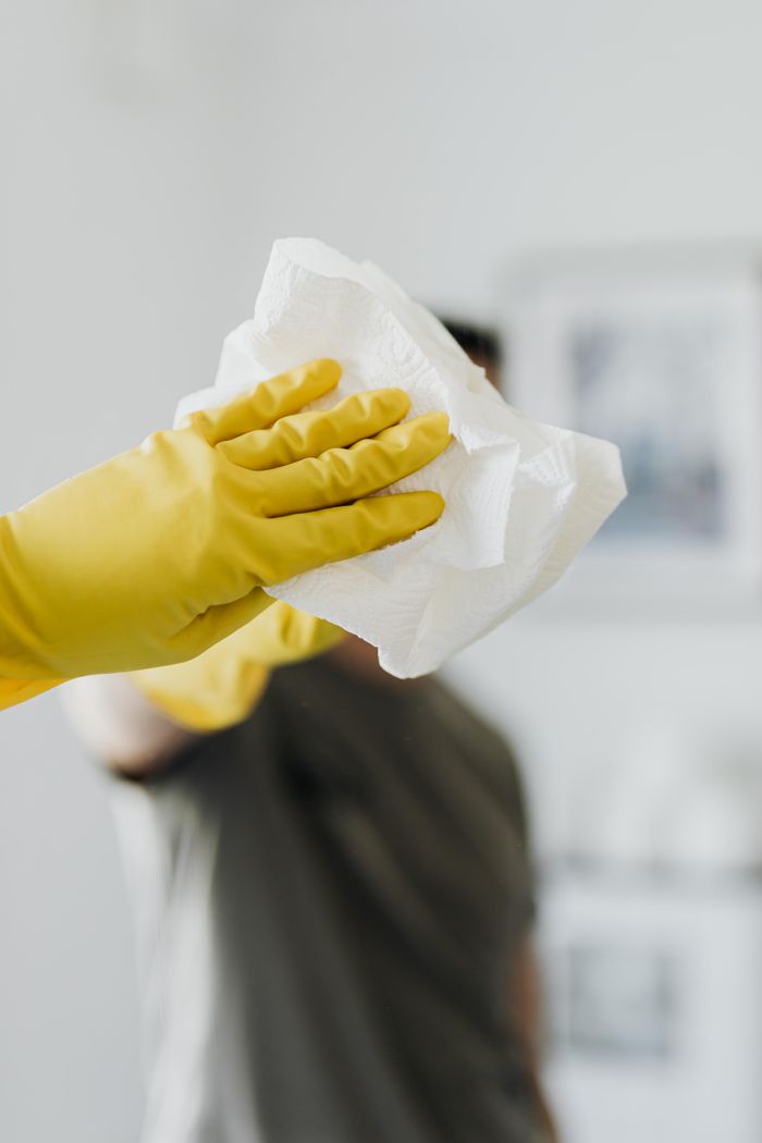 about-01 Anonymous male wearing yellow latex gloves and dark t shirt wiping mirror in bathroom with paper napkin