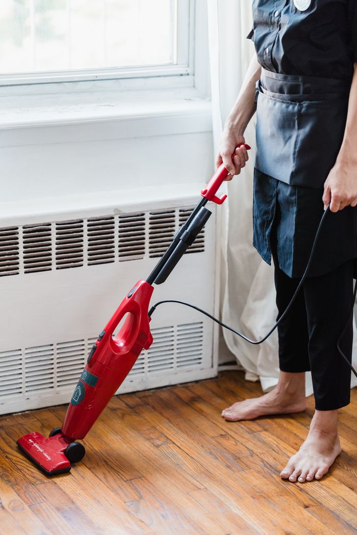 home-services-01 Person cleaning wooden floor with red vacuum cleaner in a well-lit room.
