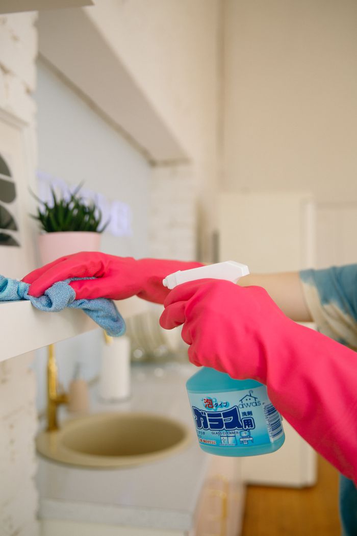 home-services-02 Person using spray bottle and cloth for cleaning a kitchen shelf, ensuring hygiene and cleanliness.