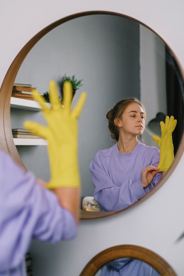 home-services-03 A woman wearing yellow gloves is reflected in a wall mirror indoors, exuding a serene expression.